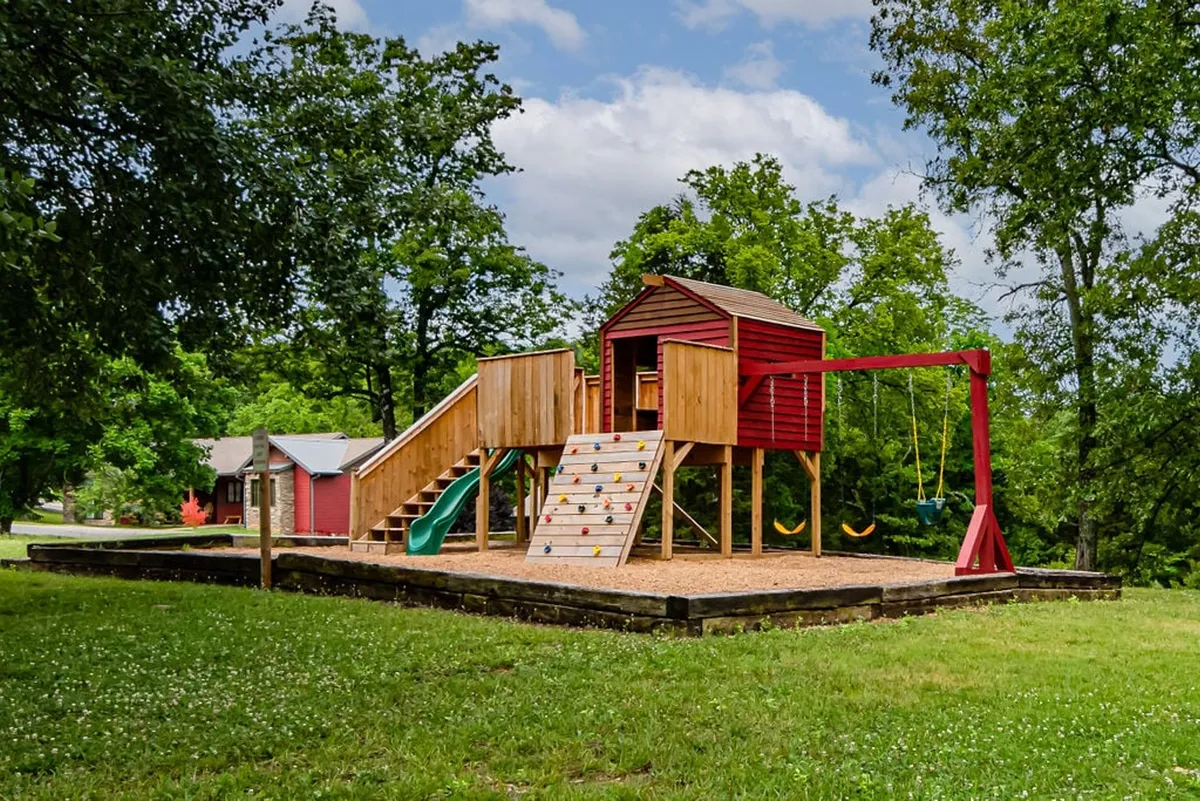 A vibrant playground with swings and a climbing wall, surrounded by lush greenery. Children can be seen enjoying the area, with plenty of space for imaginative play and activity.