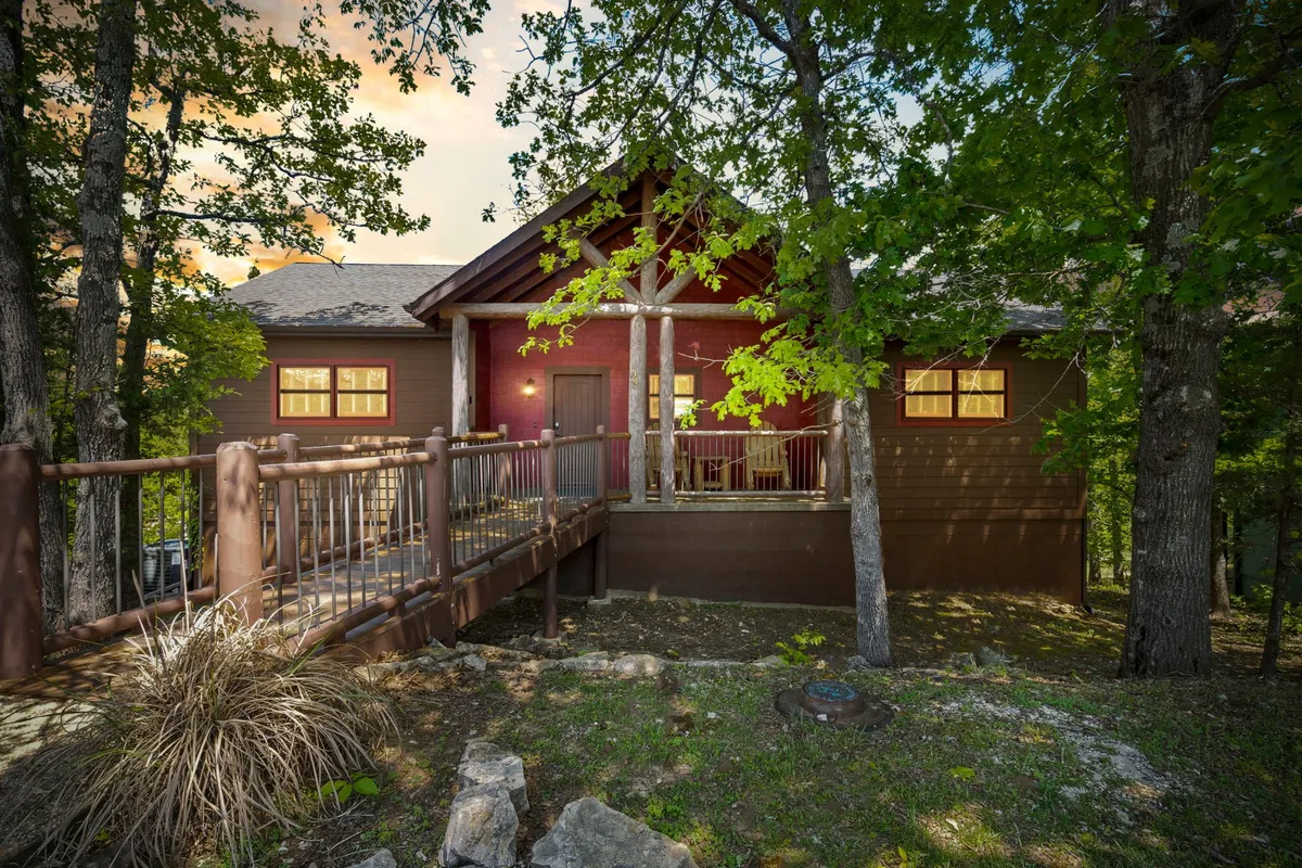 This image captures the exterior of Wickman's Fancy, featuring a welcoming wooden deck at the front entrance framed by mature trees and a stone pathway. The deck looks ideal for gatherings or a quiet morning coffee while taking in the peaceful wooded surroundings.