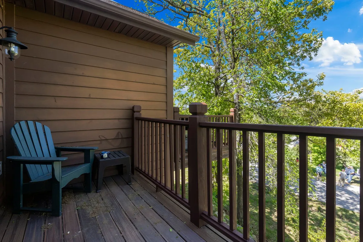 An adirondack chair and small table sit on a wooden railing deck, surrounded by trees. The setup is ideal for enjoying morning coffee, reading, or socializing with friends while immersed in nature.