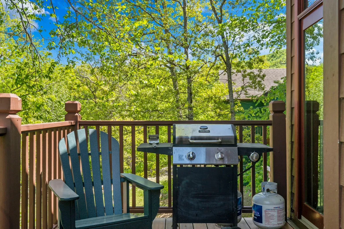 An inviting outdoor deck scene with a grill, Adirondack chair, and surrounding greenery. The setup hints at barbecuing, relaxing, and outdoor dining—activities closely tied to warm-weather fun and gatherings with friends or family.