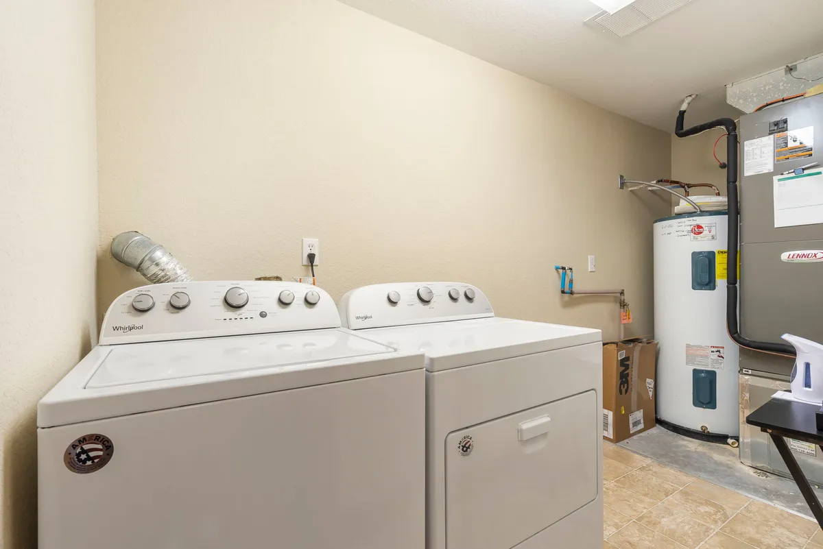 A bright, efficiently organized laundry room showcasing a washer and dryer, a water heater, and a utility cabinet. The space is functional and well-lit, emphasizing convenience and practicality for guests during their stay.