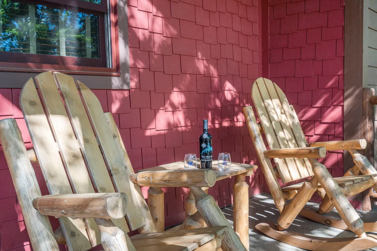 A pair of wooden rocking chairs and a bottle of wine with glasses set on a deck, surrounded by natural greenery. The scene evokes a sense of relaxation and leisurely enjoyment in a private, tranquil setting.