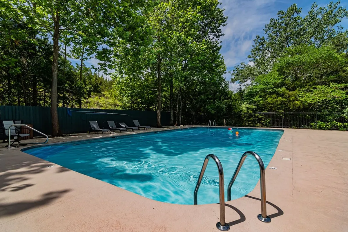 An inviting outdoor swimming pool surrounded by lush trees and poolside loungers, providing a tranquil setting for swimming, sunbathing, or relaxing with friends. The pool area captures a quintessential resort-style perk enjoyed by guests.