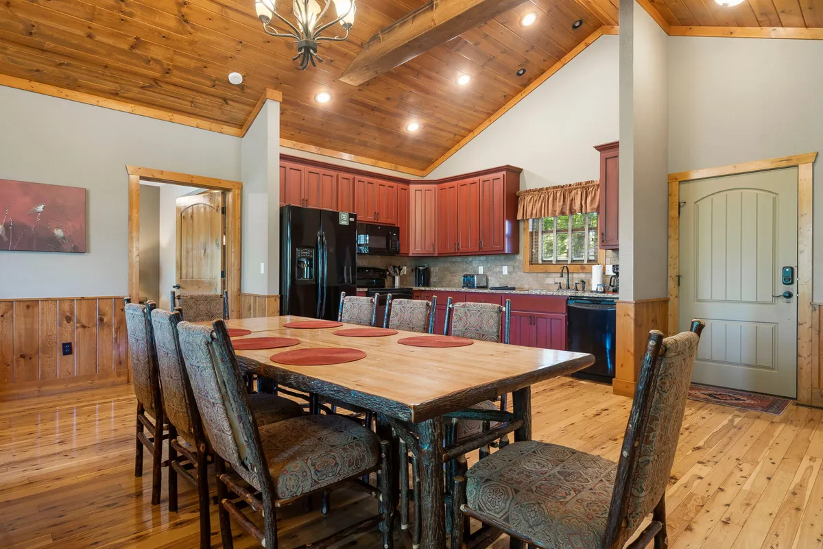 A large wooden dining table sits beneath elegant chandelier lighting, with red cabinetry in the background. The cozy setting suggests gatherings for family meals, celebrations, and heartfelt conversations, enhanced by the inviting décor and warm ambiance.