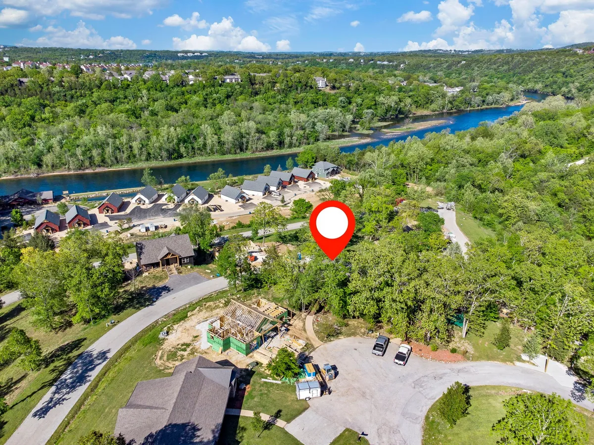 This image captures a newly constructed building along the river, surrounded by lush greenery and other homes. The scene shows people walking along the river, exploring nearby trails, and hints at a vibrant community atmosphere with potential for local events.