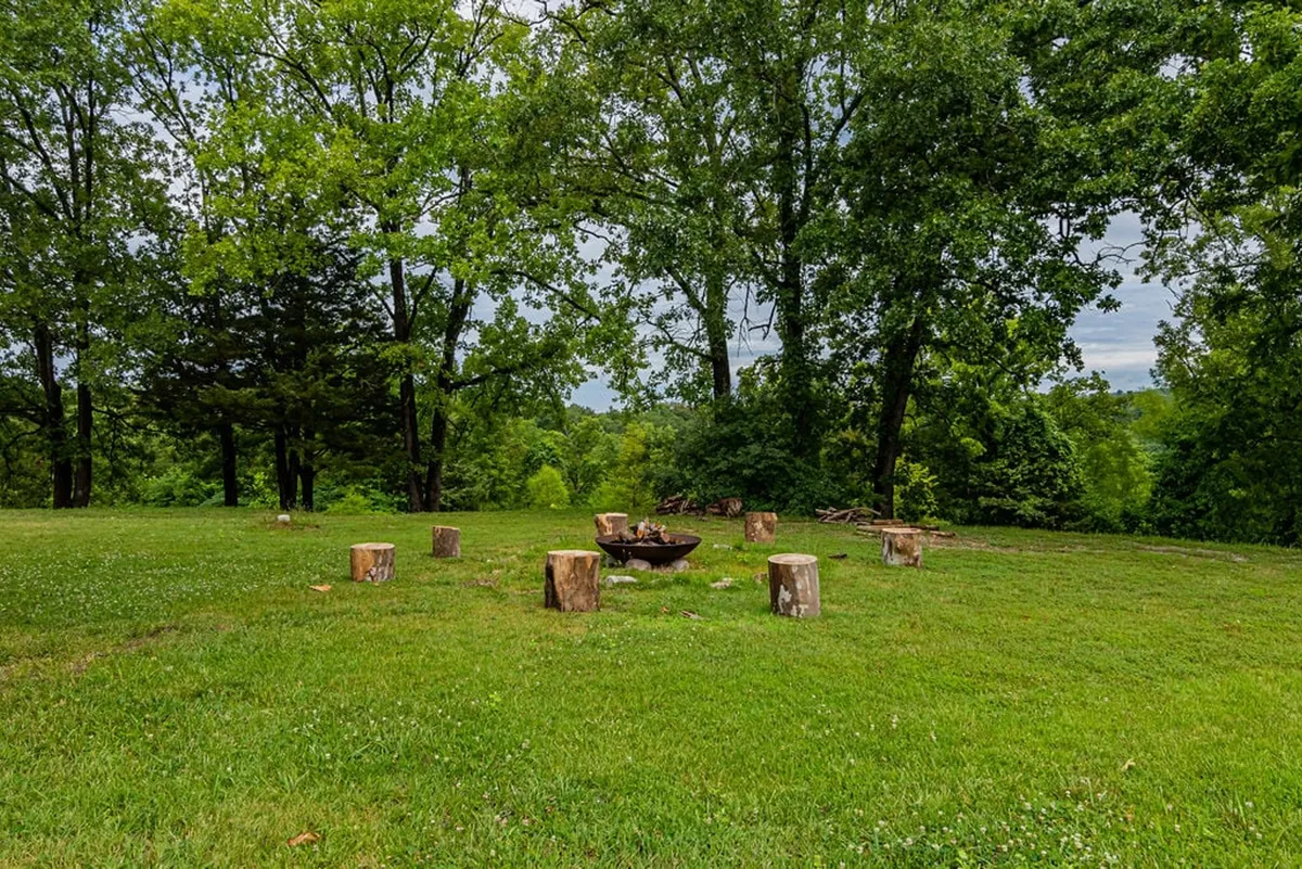 A cozy fire pit area set among trees with log seating, inviting guests to gather, share stories, or enjoy evenings under the stars. The natural setting is both social and serene, suitable for all seasons, especially cooler evenings.